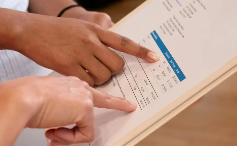 Mãos de pessoas preenchendo uma tabela de faturamento em documento impresso, com destaque para informações financeiras e valores, representando a rotina de faturamento de serviços do novo empreendedor.